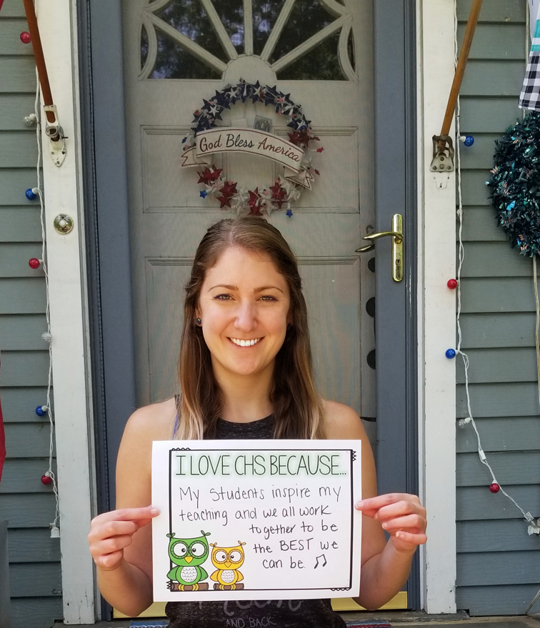 photo of blonde woman standing in front of a door with a sign that reads "I love CHS because my students inspire my teaching and we all work together to be the BEST we can be"